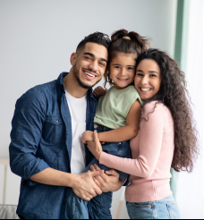 Мужчина стоит рядом с женой, держа на руках их дочь.