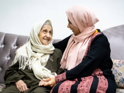 Женщина разговаривает со своей пожилой матерью, и они смеются вместе.