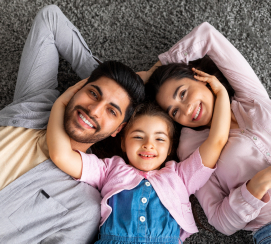 Девочка обнимает своих родителей, и они улыбаются, лежа на земле.