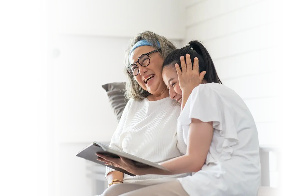Woman holding her granddaughter and laughing while looking at a photo album