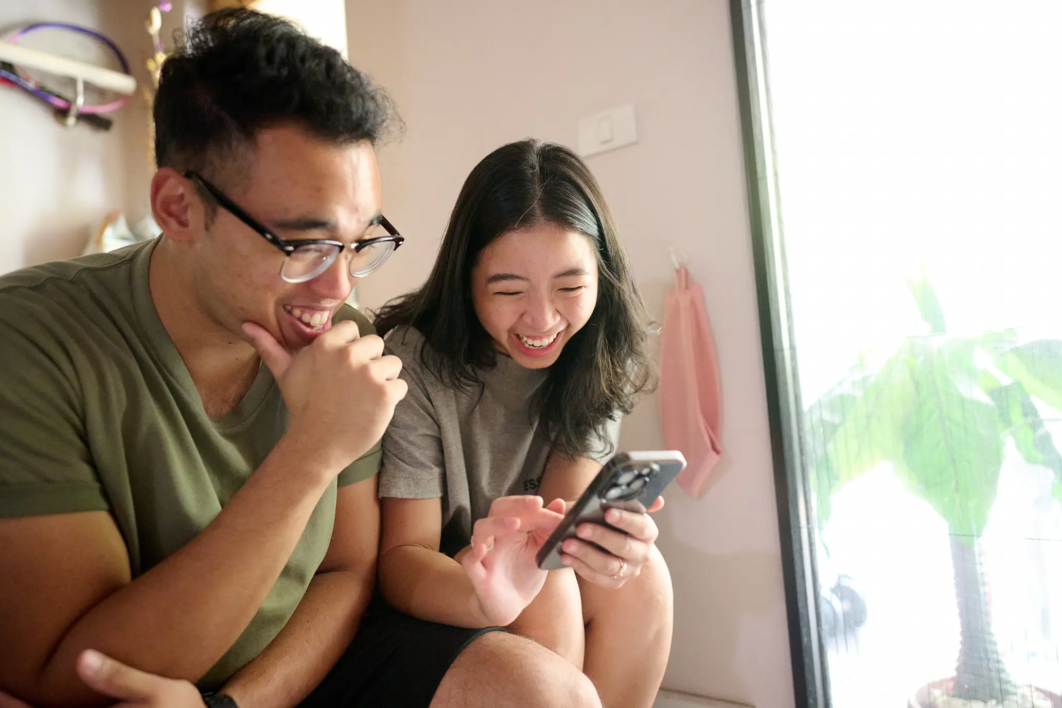 A man smiles as a woman sitting next to him shares a family history discovery on her phone.